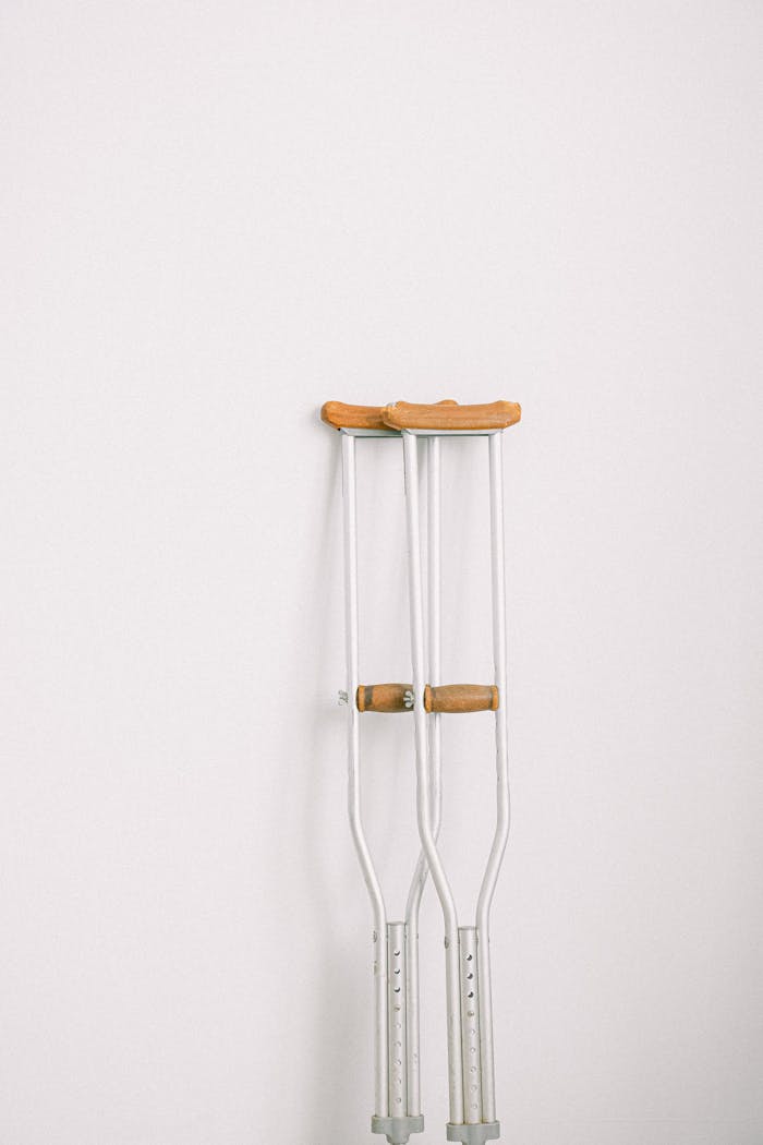 Minimalist image of crutches leaning on a white wall indoors.